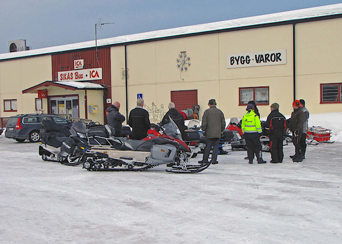 Grupp med snöskotrar och personer utanför en Ica-butik vintertid