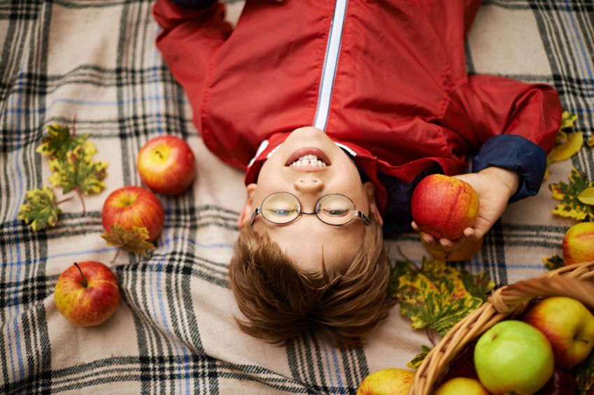 little boy lying on blanket rounded by leafs and apples