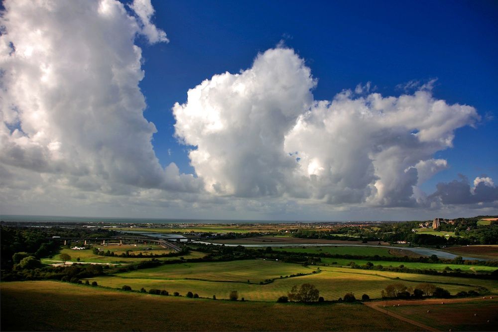 Stora vita moln ovanför landsbygdslandskap.