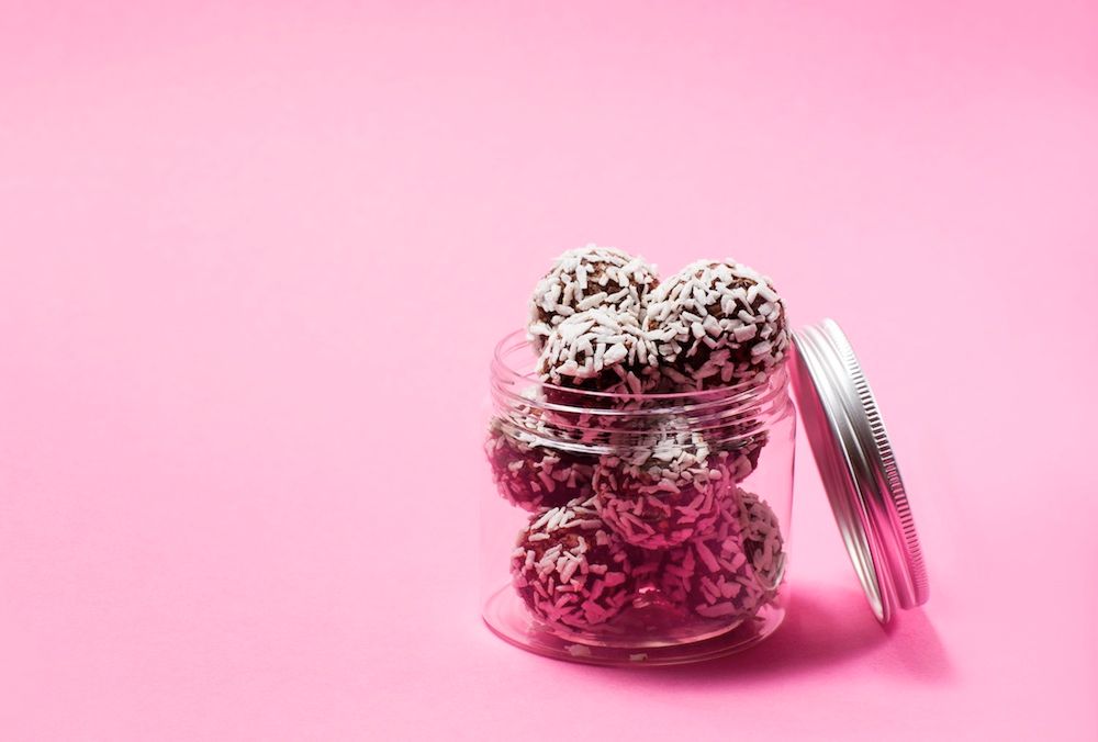 Glasburk med chokladbollar rullade i kokos på rosa bakgrund