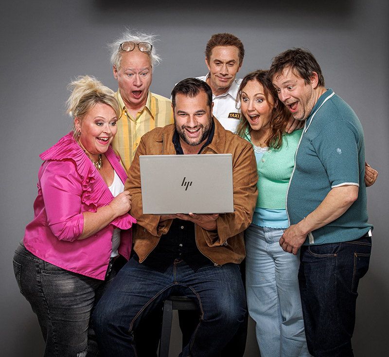 Sex personer står samlade och tittar glatt och förvånat på en bärbar dator