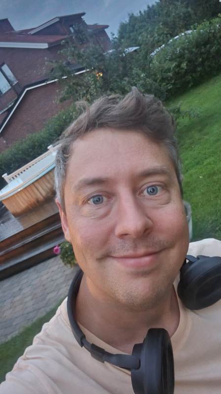 Leende man  i trädgård framför ett hus i kvällsljus