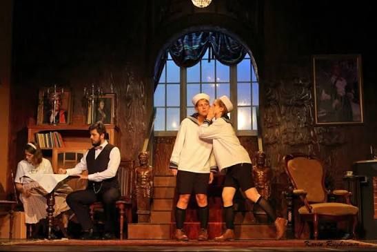 Teaterscen där två pojkar i sjömanskläder omfamnas, med vuxna sittande bredvid