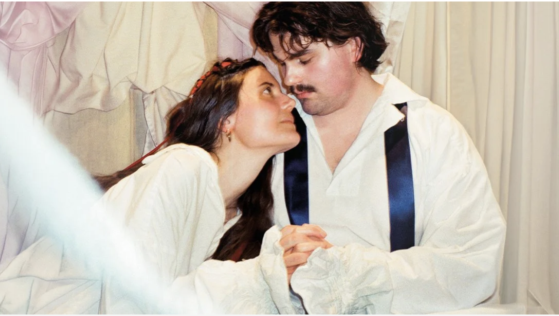 Två personer i historiska kläder håller händerna och ser kärleksfullt på varandra