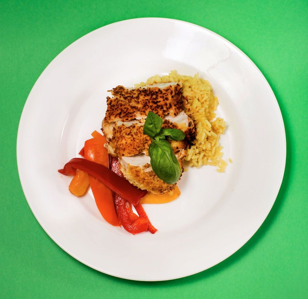 Panerad kyckling med ris och paprika på vit tallrik mot grön bakgrund