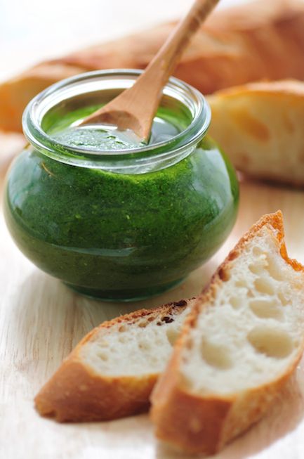 Liten glasburk med grön pesto intill ligger två ljusa brödbitar.