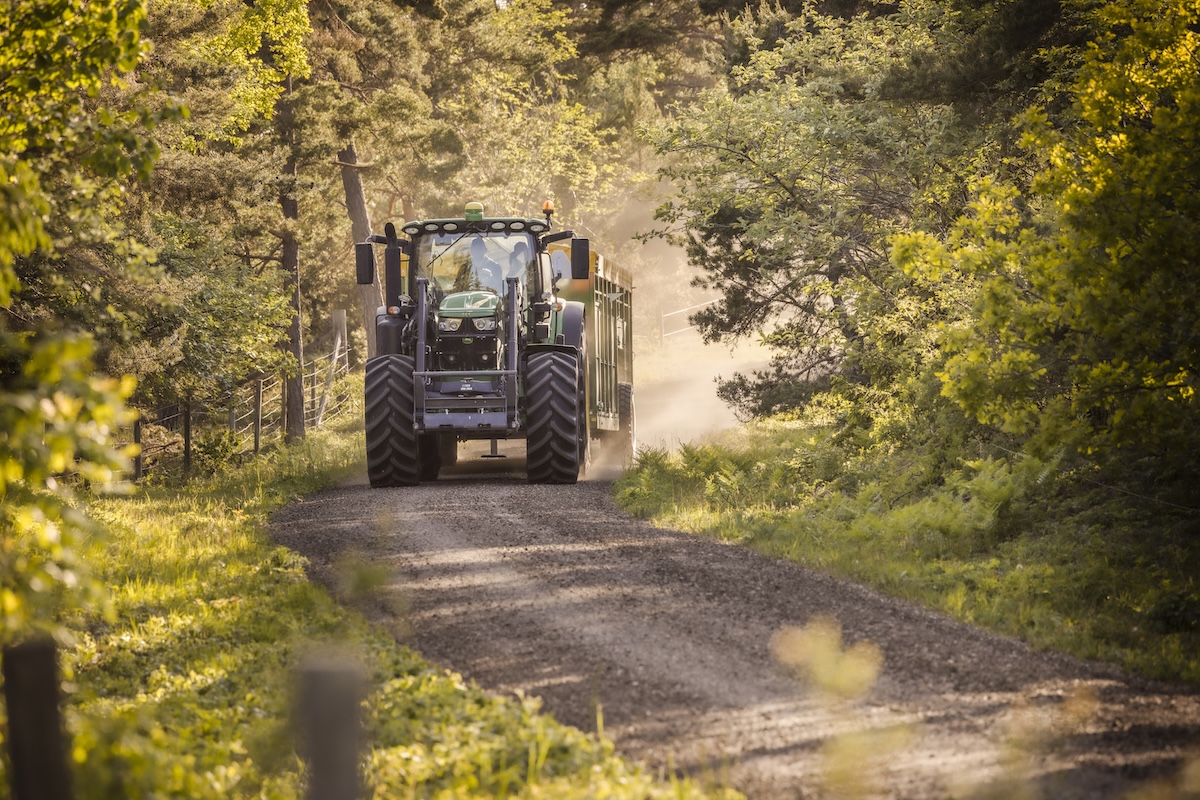 Traktor som kör längs en skogsbeklädd grusväg