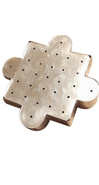Metallplatta formad som pusselbit med små borrade hål på ytan