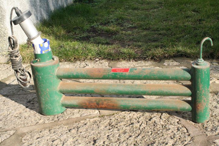 Grön rostig metallanordning med elkabel, liggande på stenplattor utomhus