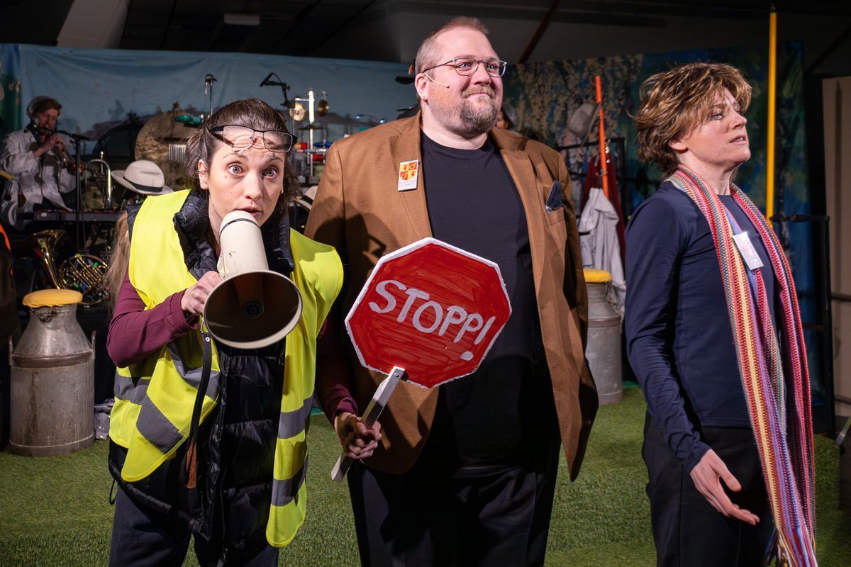 Tre skådespelare på scen, en med megafon och en med stopp-skylt som det står STOPP! på