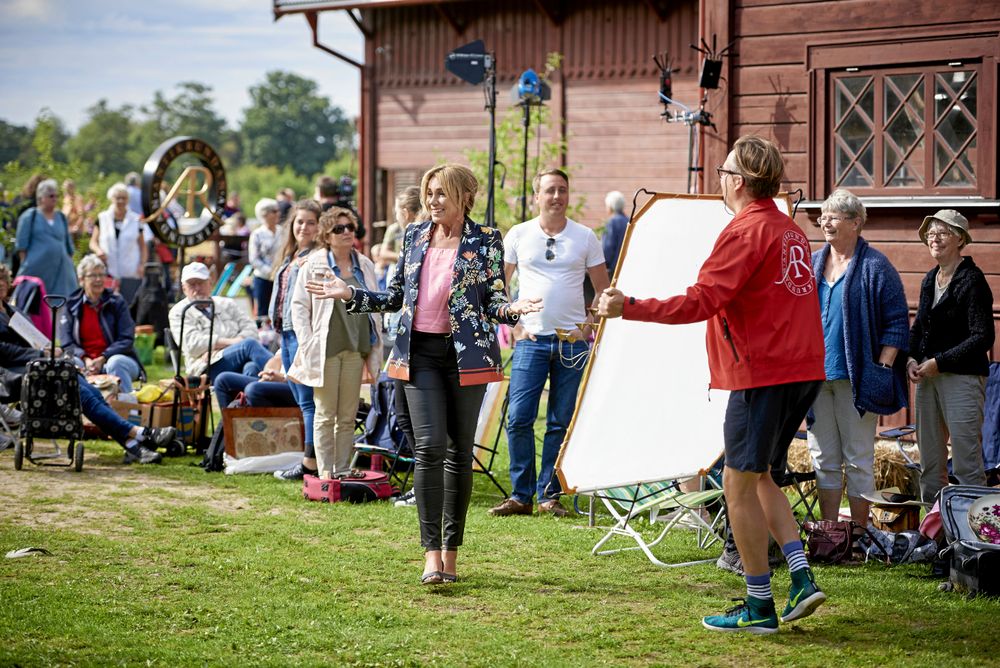Inspelning utomhus med programledare framför publik vid röd träbyggnad