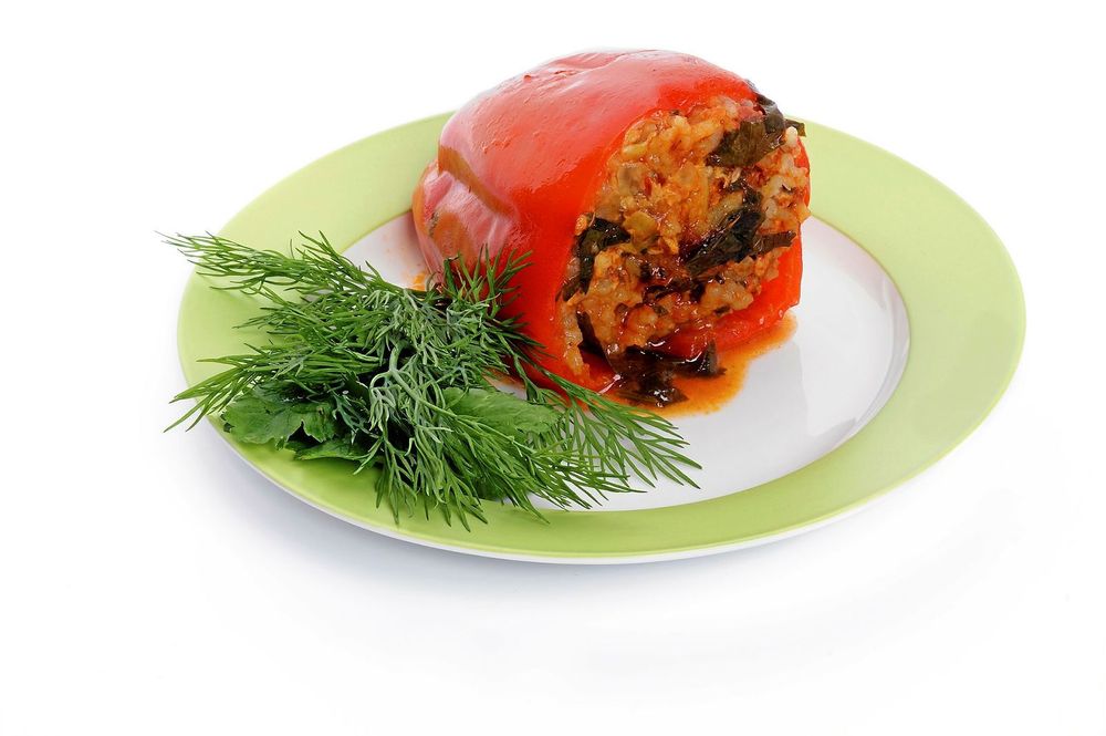Homemade Red Bell Pepper Filled with Rice, Meat, Onion and Parsley on green plate isolated on white background