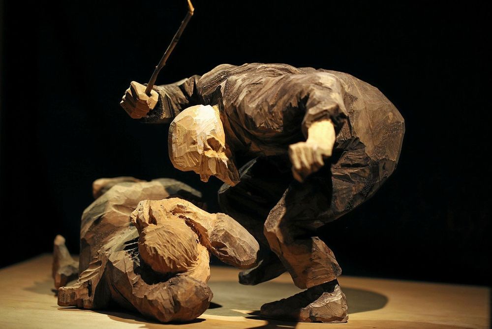 En träfigur där en man ser ut att slå en kvinna som ligger ner. Snidad av Döderhultarn.