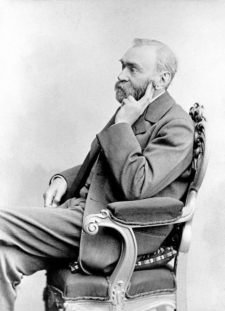 Svartvitt foto på Alfred Nobel i profil, iklädd kostym och sittandes i en utsmyckad stol.