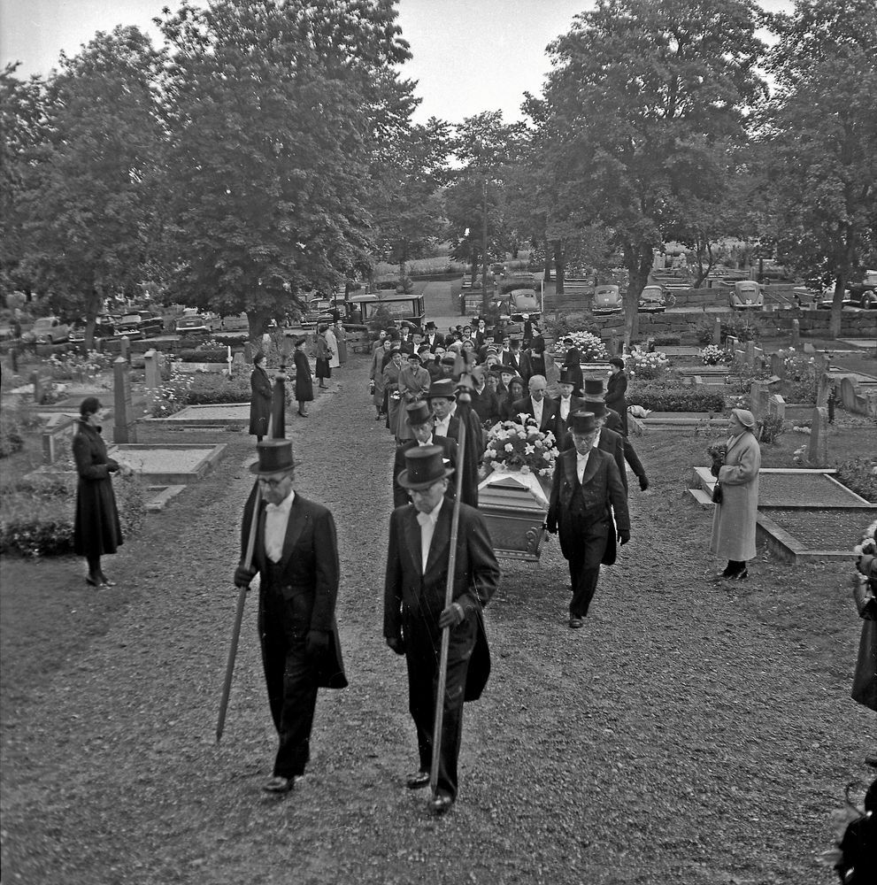 Svartvit bild av ett begravningståg, där sex personer bär kistan på väg mot Kville kyrka.