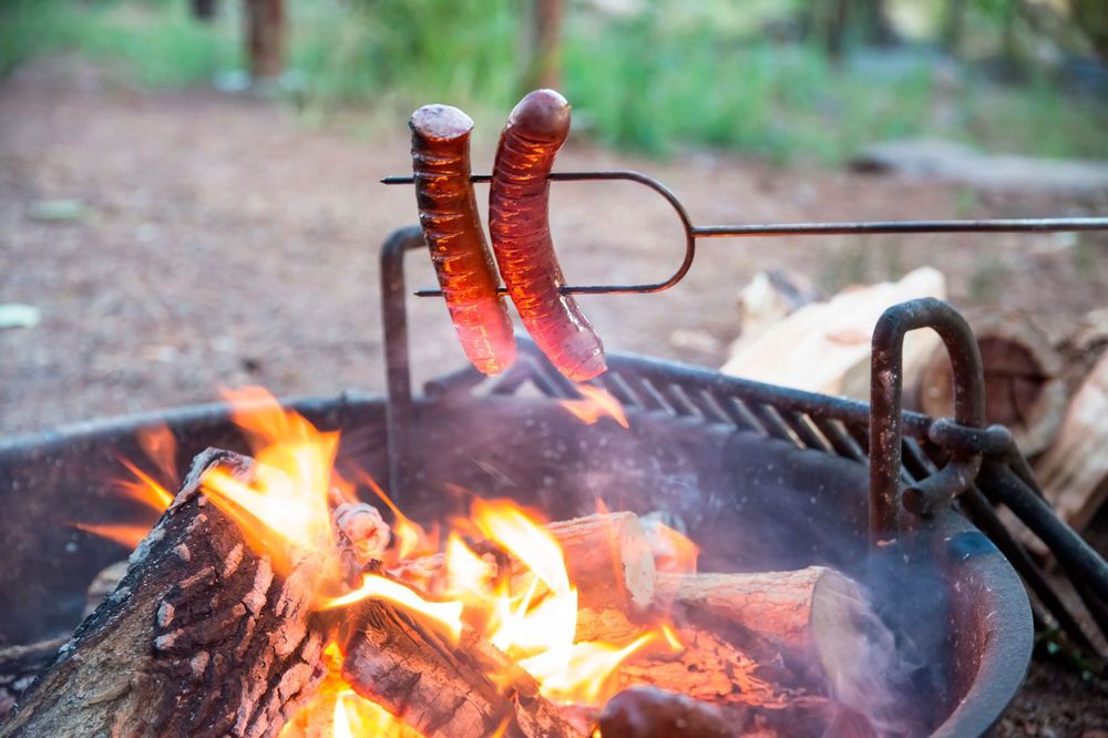 Två grillkorvar på spett i grill. 