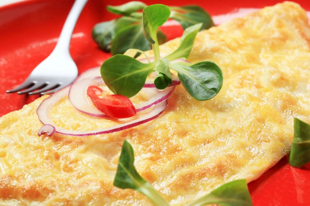 Omelett på röd tallrik toppad med sallad, rödlök och röd chili