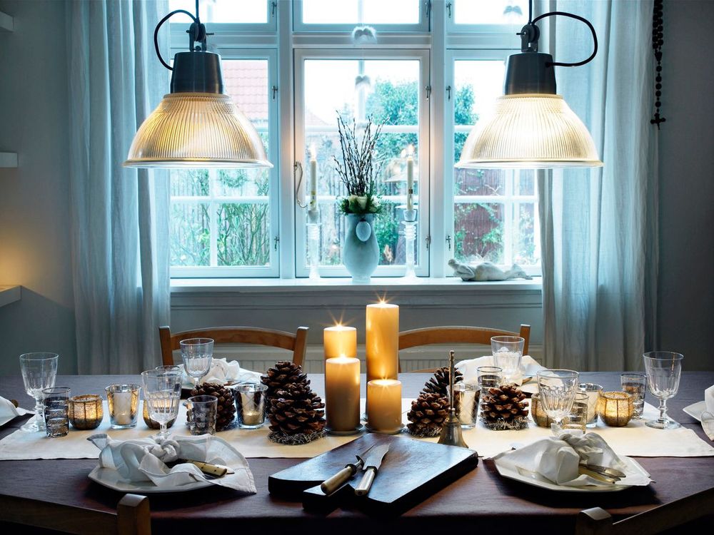 Vinterdukad matplats med tända ljus, glas och kottdekorationer vid ett fönster