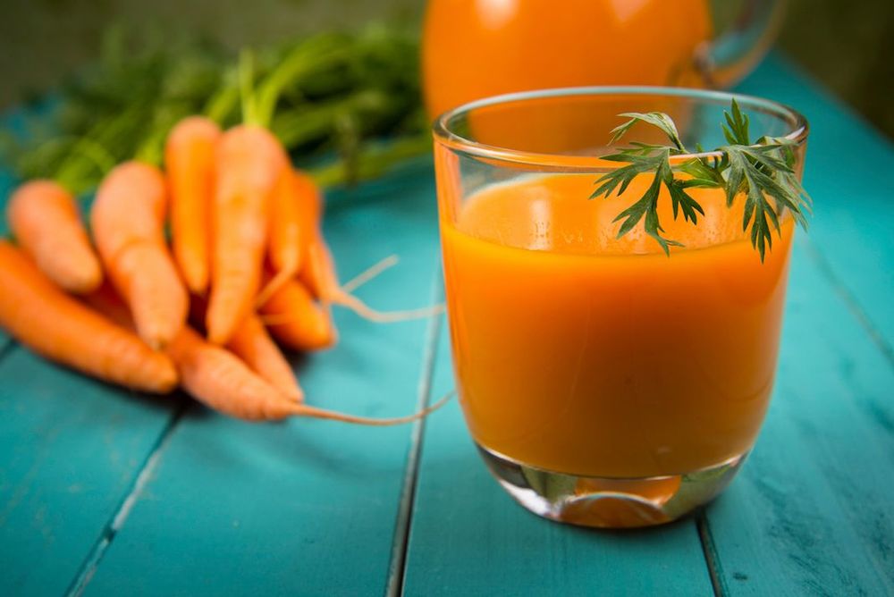 Glas med morotsjuice på ett turkost träbord. En knippe morötter ligger bredvid.