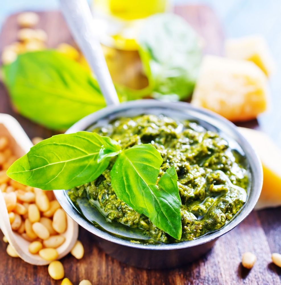 Skål med grön pesto, färsk basilika, pinjenötter och ost på en träbricka