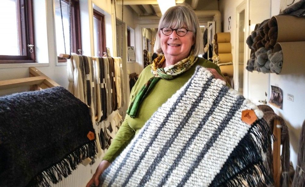 "Den här är skön att ha på kalla golv." Marianne Fröberg visar upp en ullmatta som är vävd i spinneriets vävstuga. Mattorna görs av volontärer och säljs i den egna butiken.