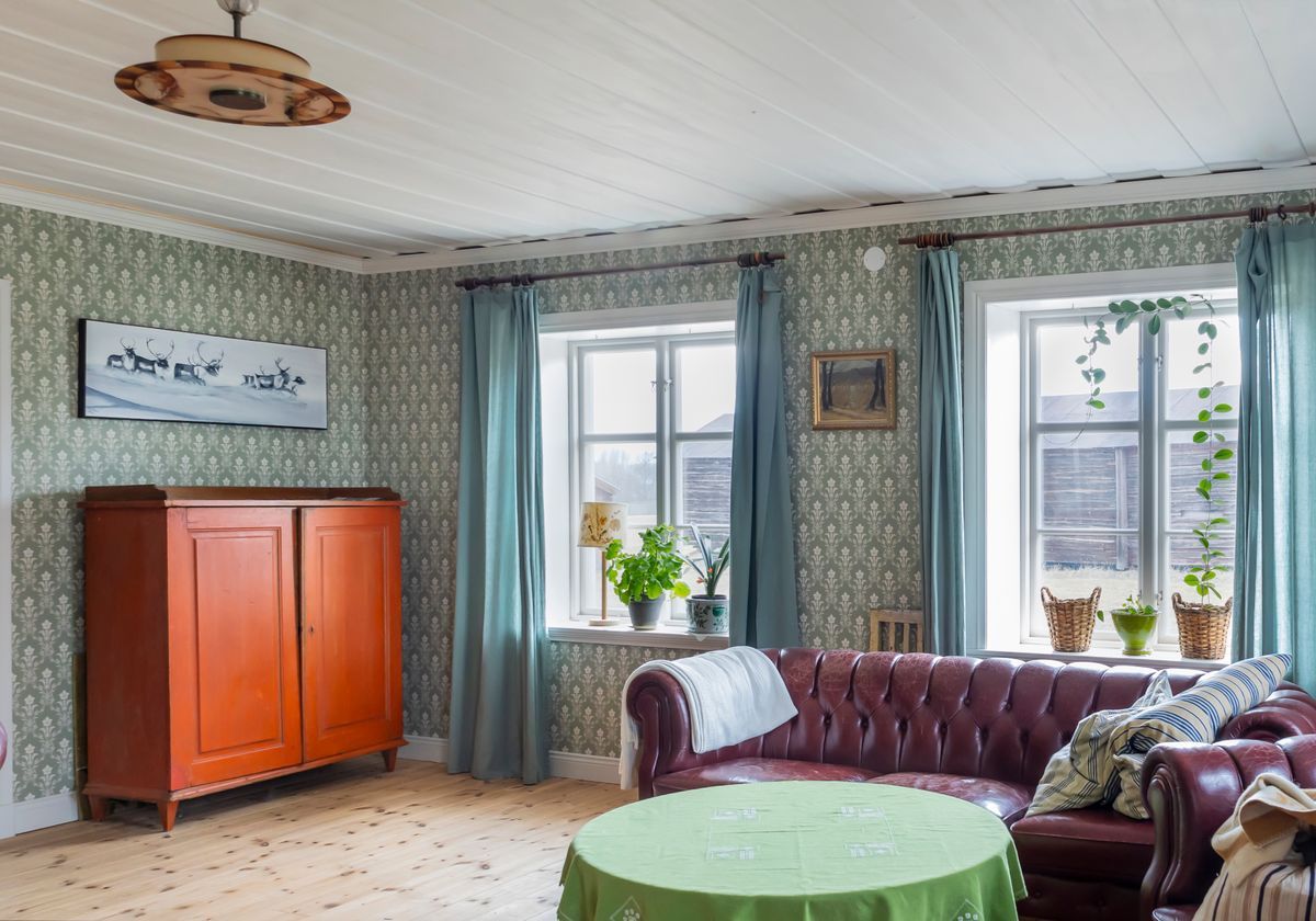 Lantligt vardagsrum med röd soffa, orange skåp och gröna gardiner
