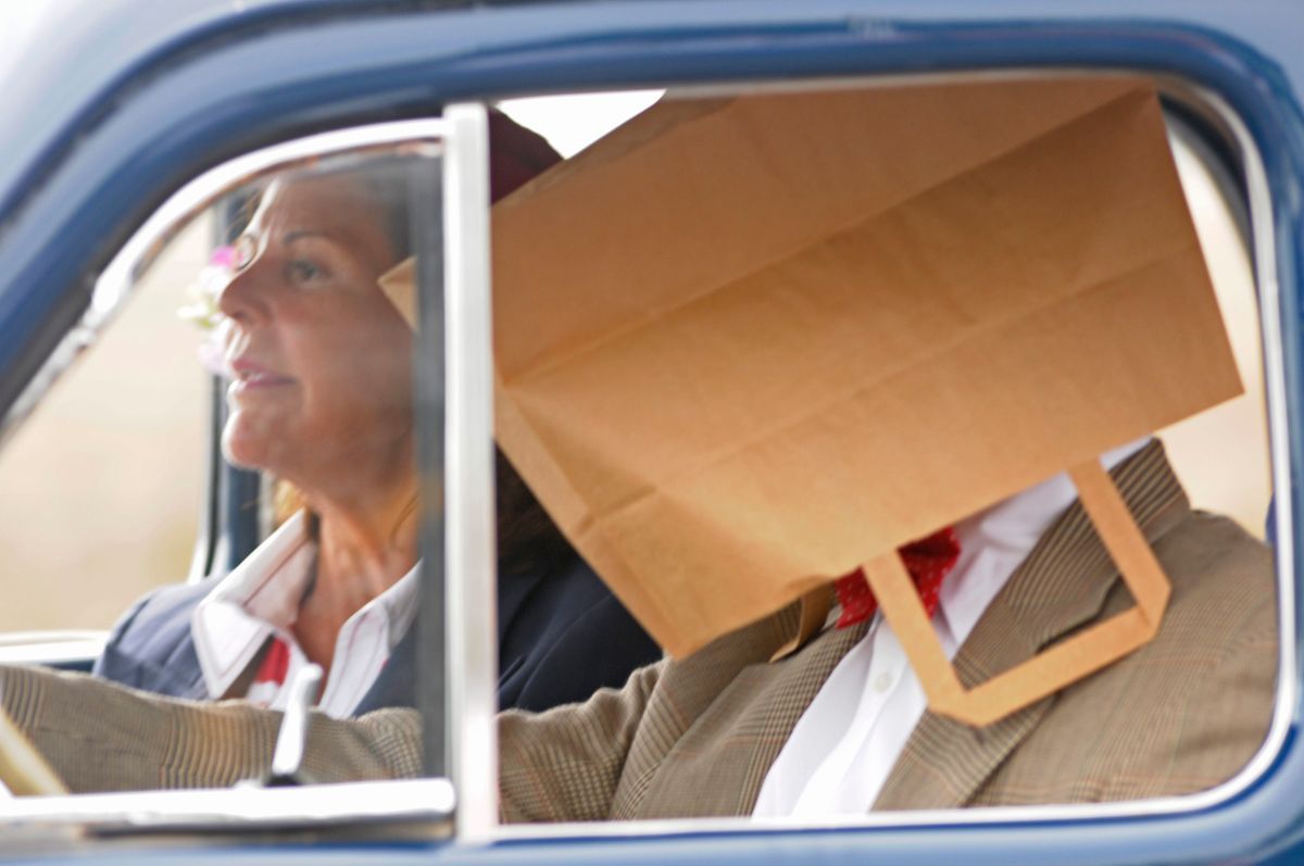 Drottning Silvia och kung Carl Gustaf i bil, kungen döljer ansiktet i papperspåse