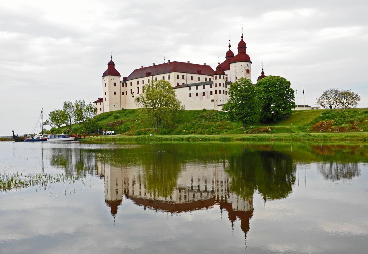 Stort slott vid en sjö med tydlig spegelbild i vattnet under mulen himmel