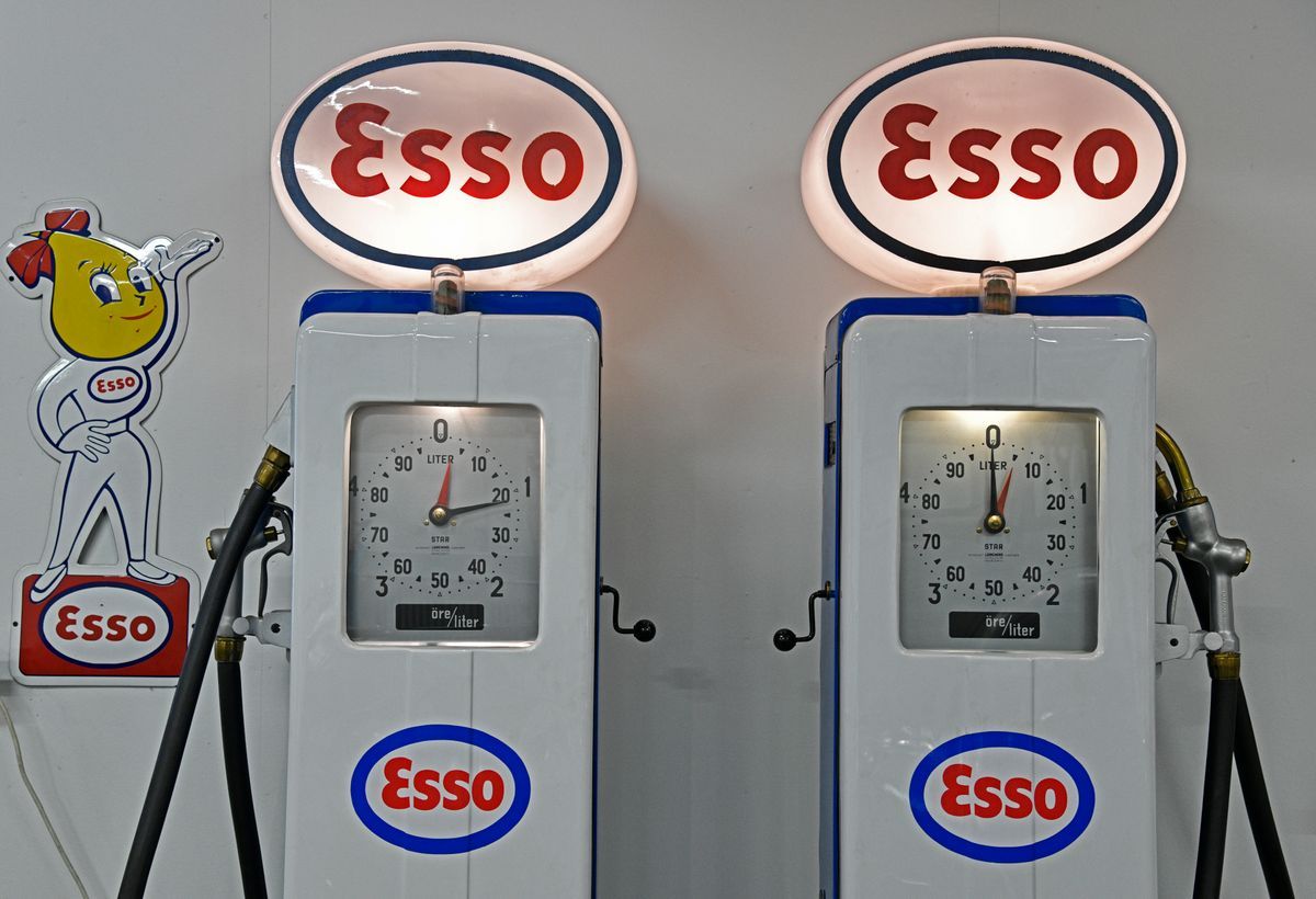 Två retro Esso-bensinmackar mot vit vägg med Esso-skylt och figur