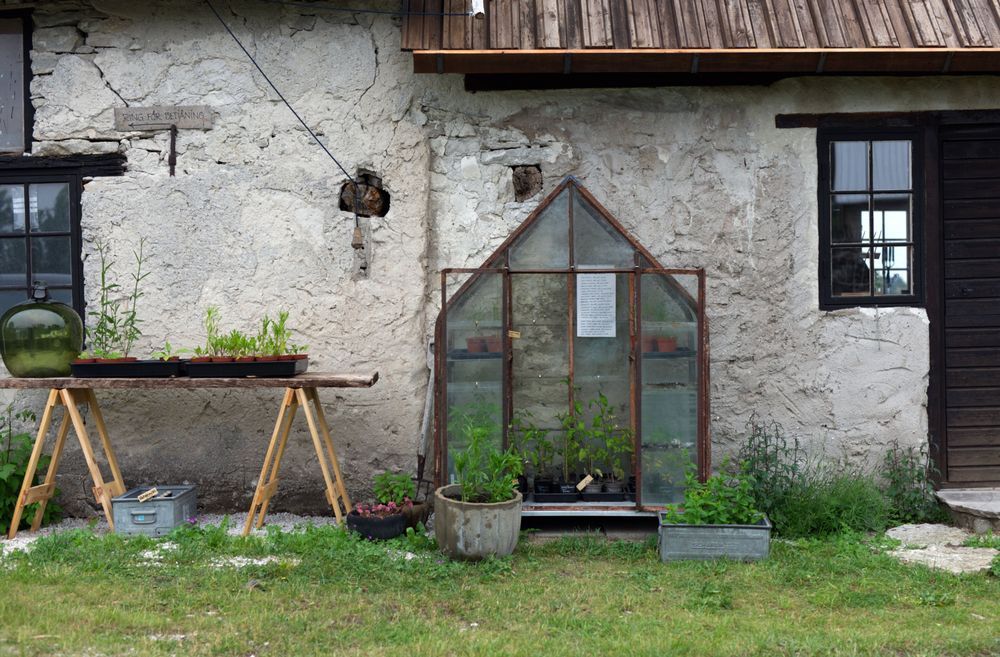 Litet växthus och plantbord mot gammal putsad husvägg på landet