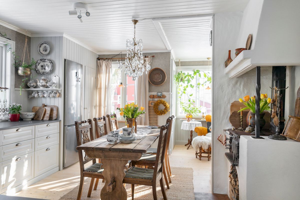 Ljus lantlig köks- och matsal med träbord, kristallkrona och vårblommor