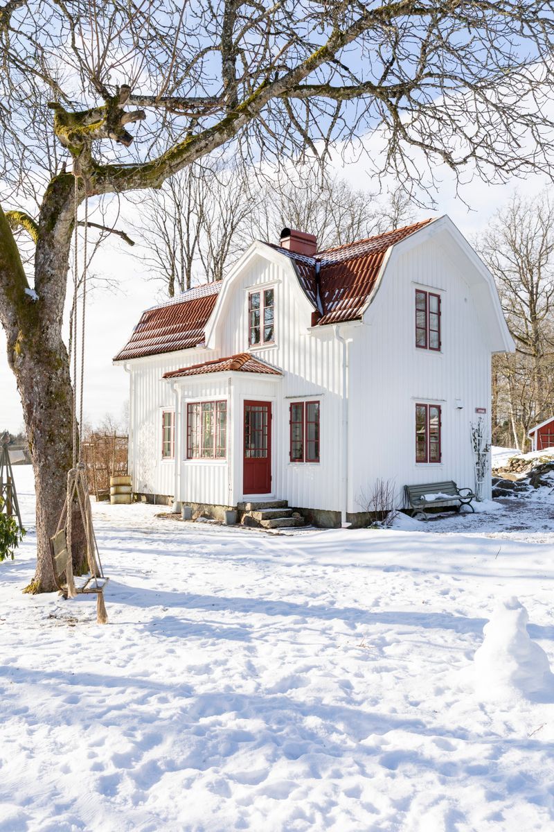 Vitt trähus med rött tak i snötäckt trädgård med trädgunga en solig vinterdag