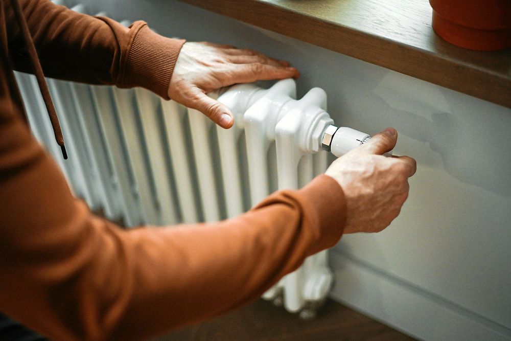 En person justerar temperaturen på ett vitt element under ett träfönsterbräda.