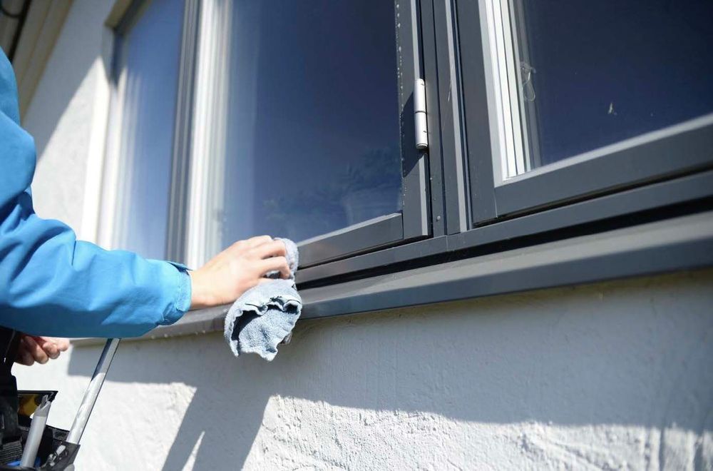 Hand torkar rent ett fönster med trasa på en vit husfasad