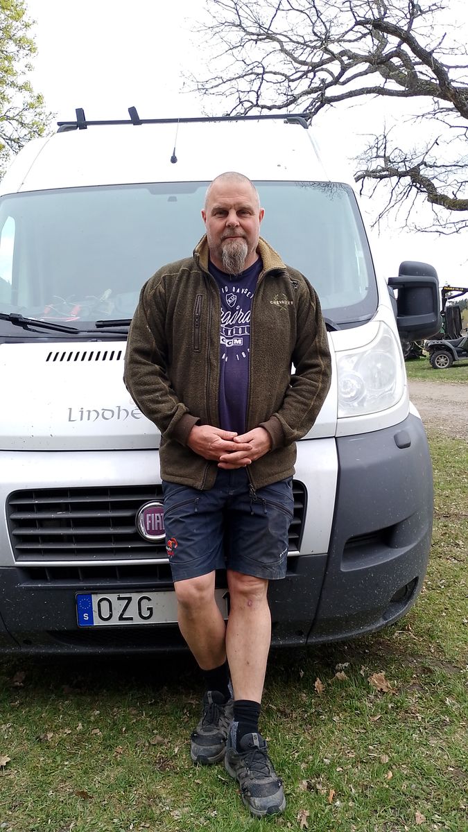 Skäggig man står framför en vit skåpbil utomhus på gräsplan