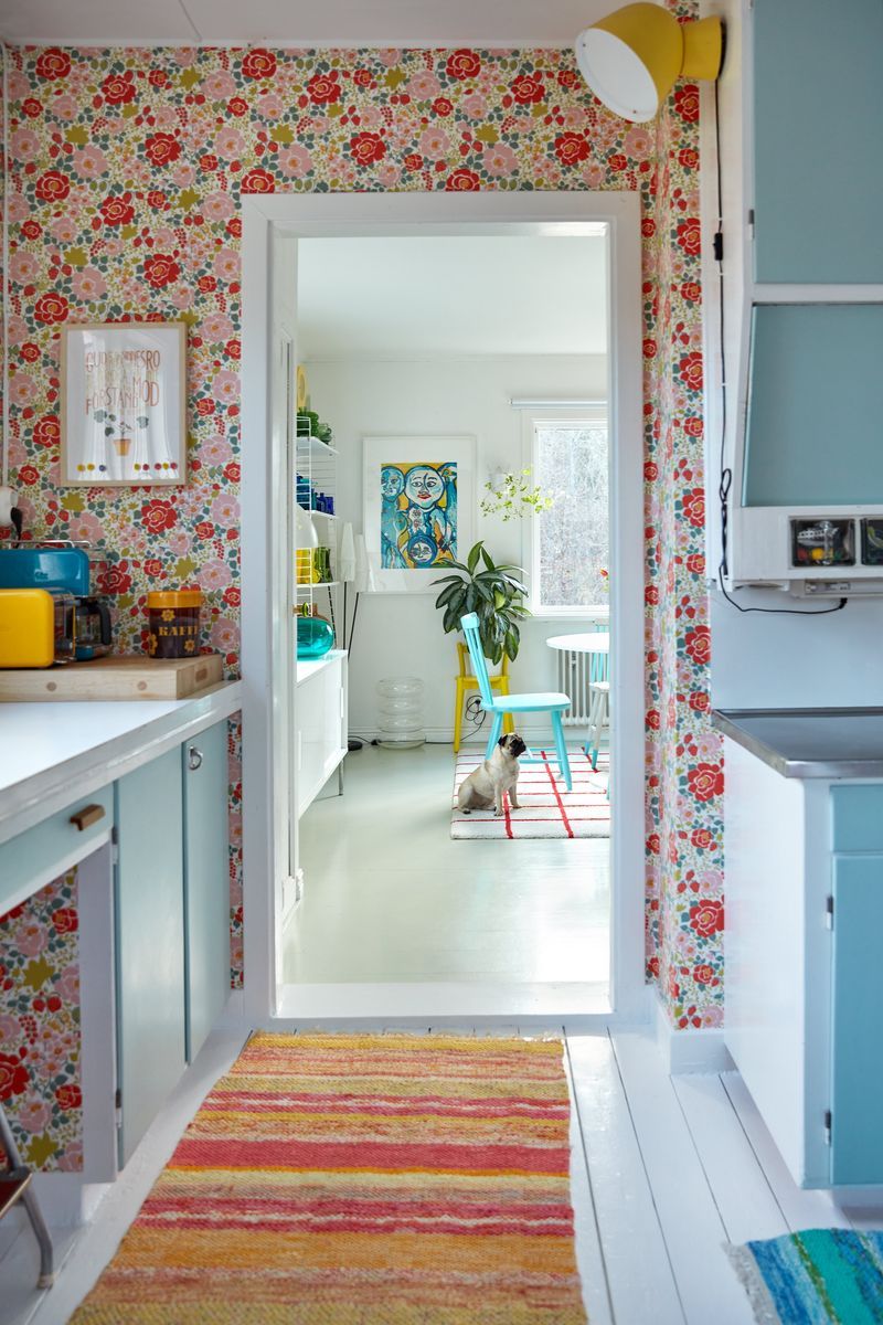 Färgglad retrokök med blommig tapet och vy mot ljust rum där en mops sitter