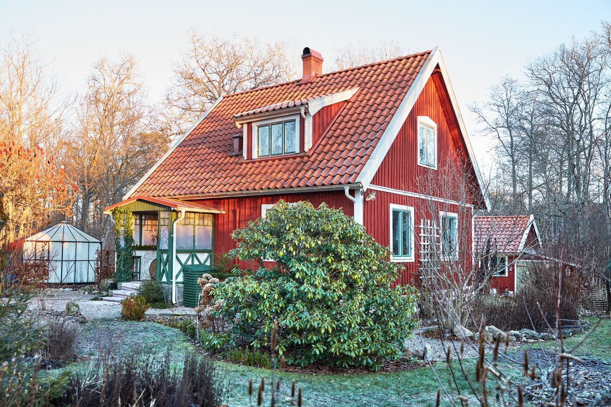 Traditionellt rött svenskt hus med trädgård och växthus en frostig morgon