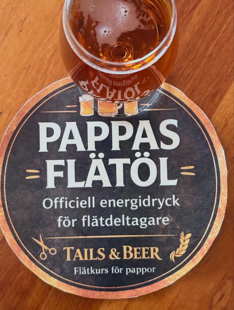 Glas öl på ölbricka med texten: Pappas flätöl – officiell energidryck