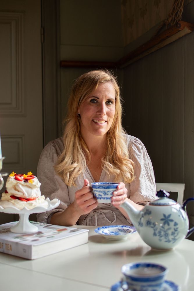 Leende kvinna vid bord med tekopp, tekanna och bakverk i dagsljus