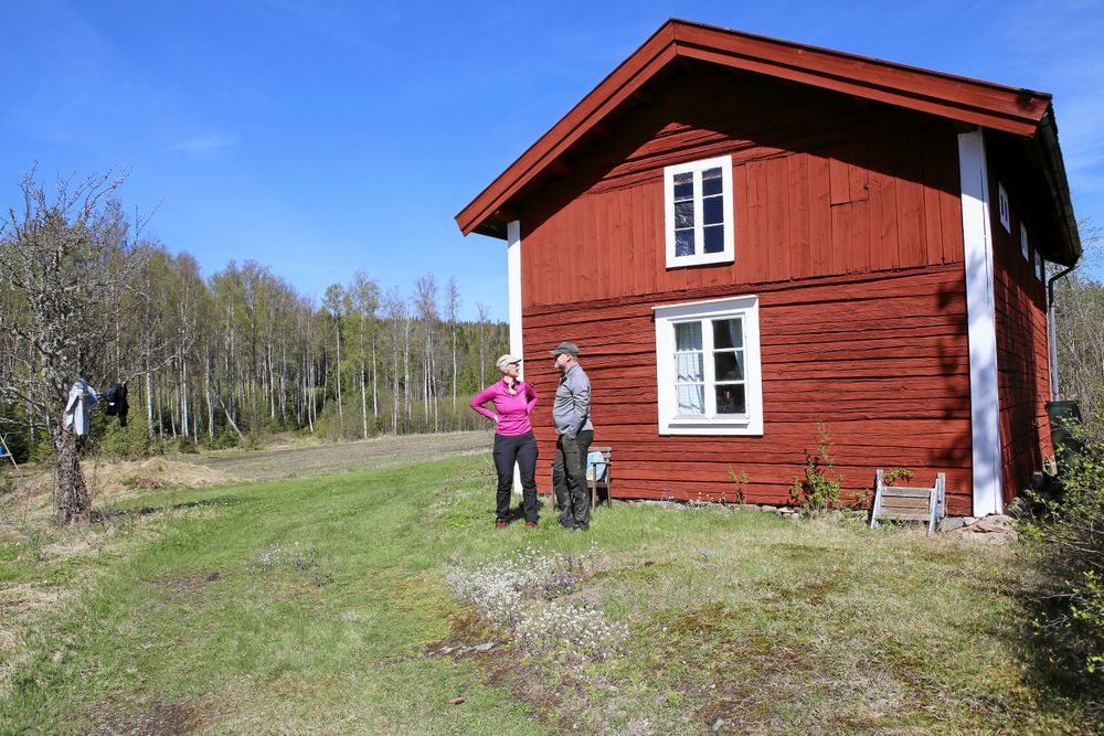 Två personer samtalar vid en röd stuga på landet.