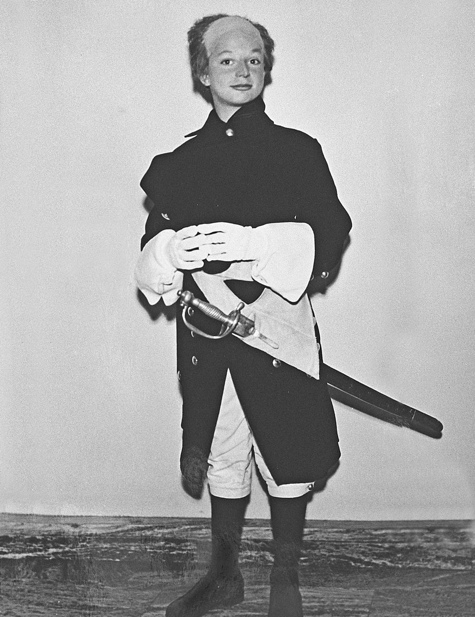 Kungen i historisk uniform med värja, poserar mot enkel bakgrund, svartvitt foto