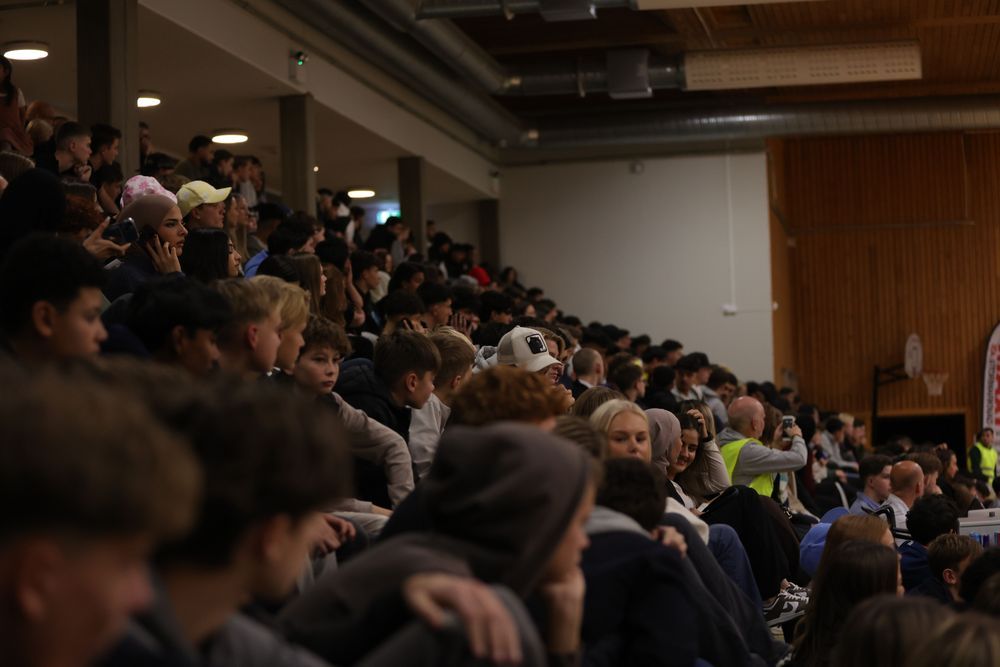 Publik sitter i läktaren under en inomhusevenemang.