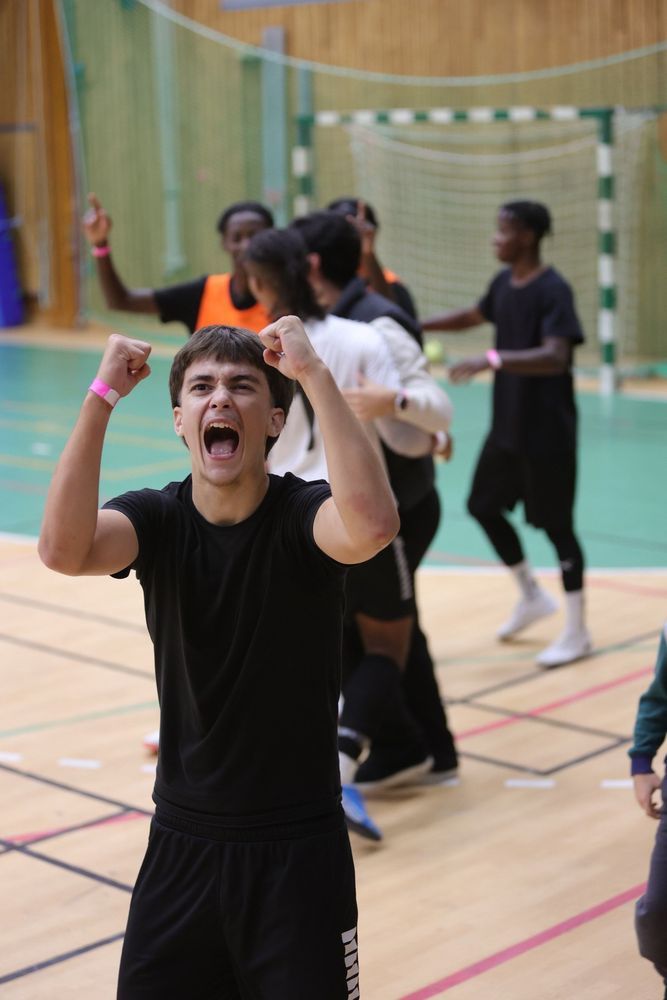 Ung man jublar i sporthall, andra spelare i bakgrunden.