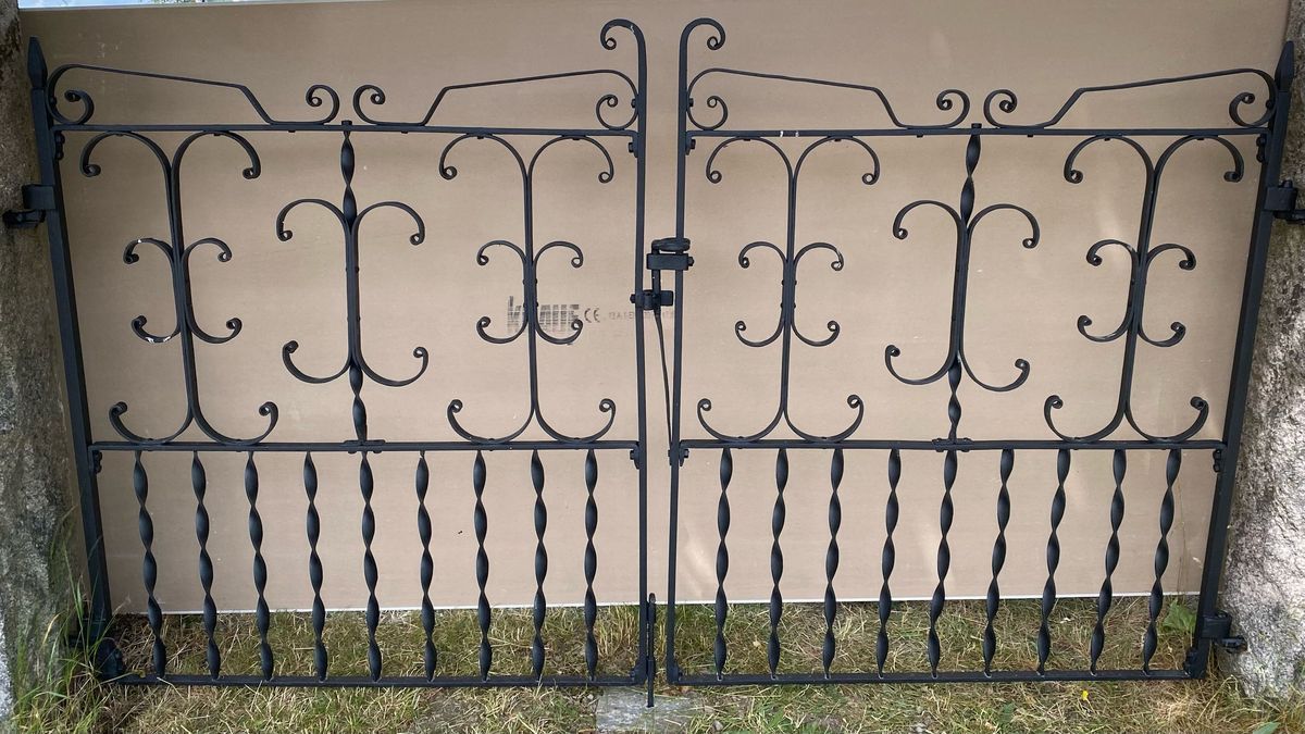 Svart smidesgrind med dekorativa mönster framför en beige bakgrund