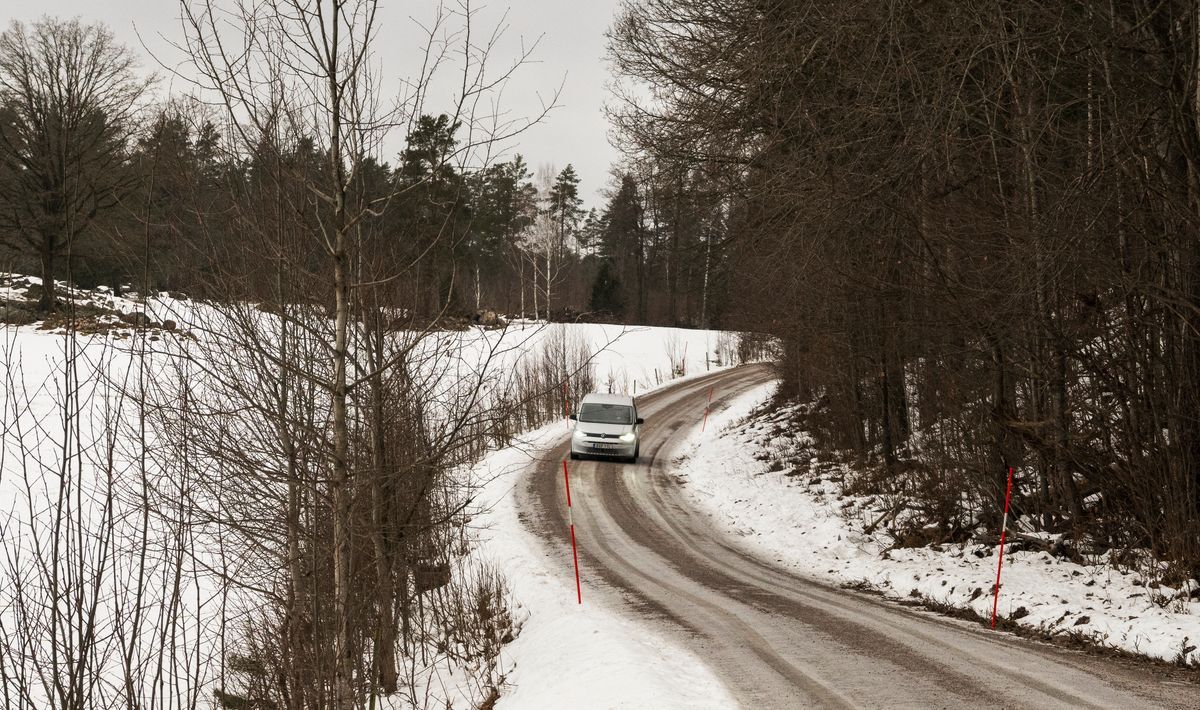 Bil kör på slingrande vinterväg genom snötäckt landskap med träd på sidorna