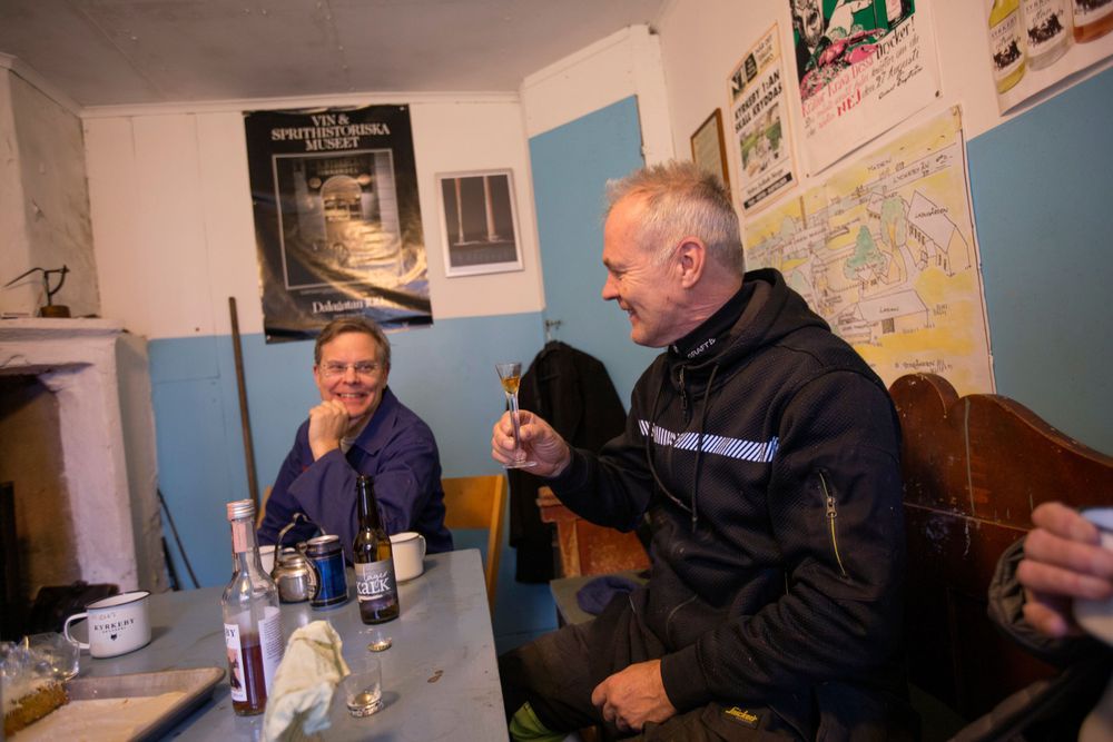 Ola Gustavsson och Torgny Arnesson  sitter vid ett bord och Torgny skålar med ett snapsglas.
