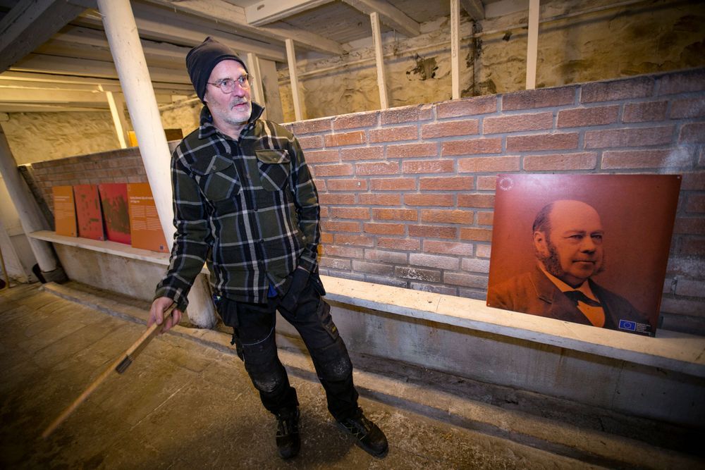 Joakim Haraldsson i mössa pekar på en tegelvägg med en bild av en historisk figur.