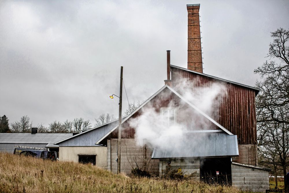 Gammal tegelbyggnad med rökpelare mot molnig himmel.