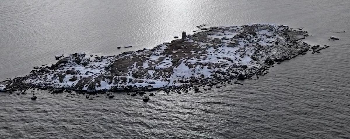 Liten snötäckt klippö omgiven av mörkt hav, sedd från luften