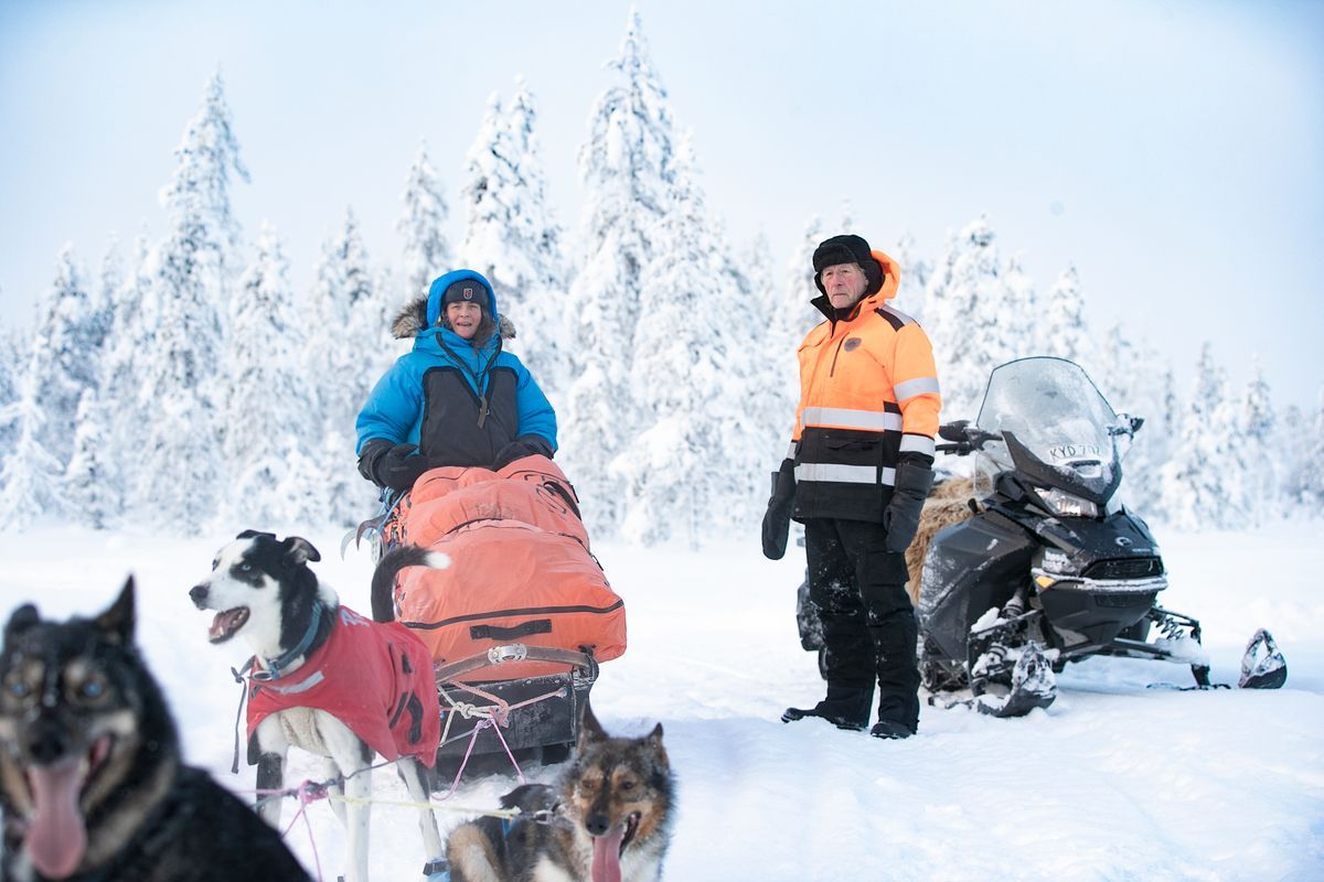 Två personer med hundspann och snöskoter i snötäckt vinterlandskap